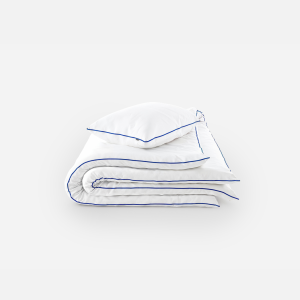 Folded white duvet and pillow set with navy blue piping on a light background, ready to use for bed bedding.